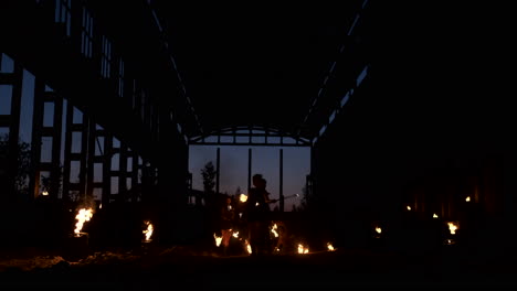 A-group-of-people-with-fire-and-torches-dancing-at-sunset-in-the-hangar-in-slow-motion.-Fire-show.